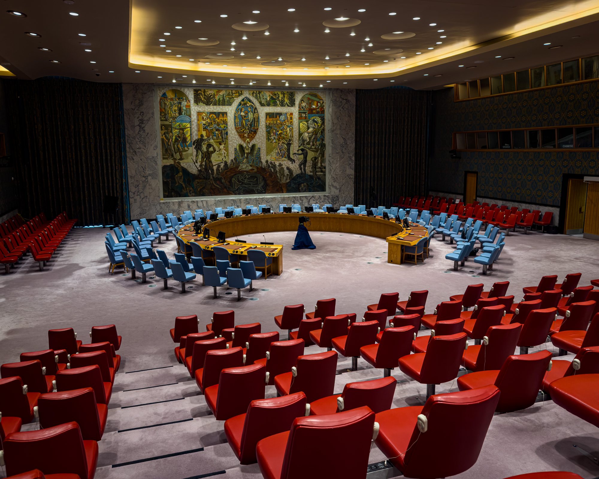 The UN Security Council chamber in New York with nobody in it: rows of empty red seats before the horseshoe table, and Per Krohg's mural on the far wall.
